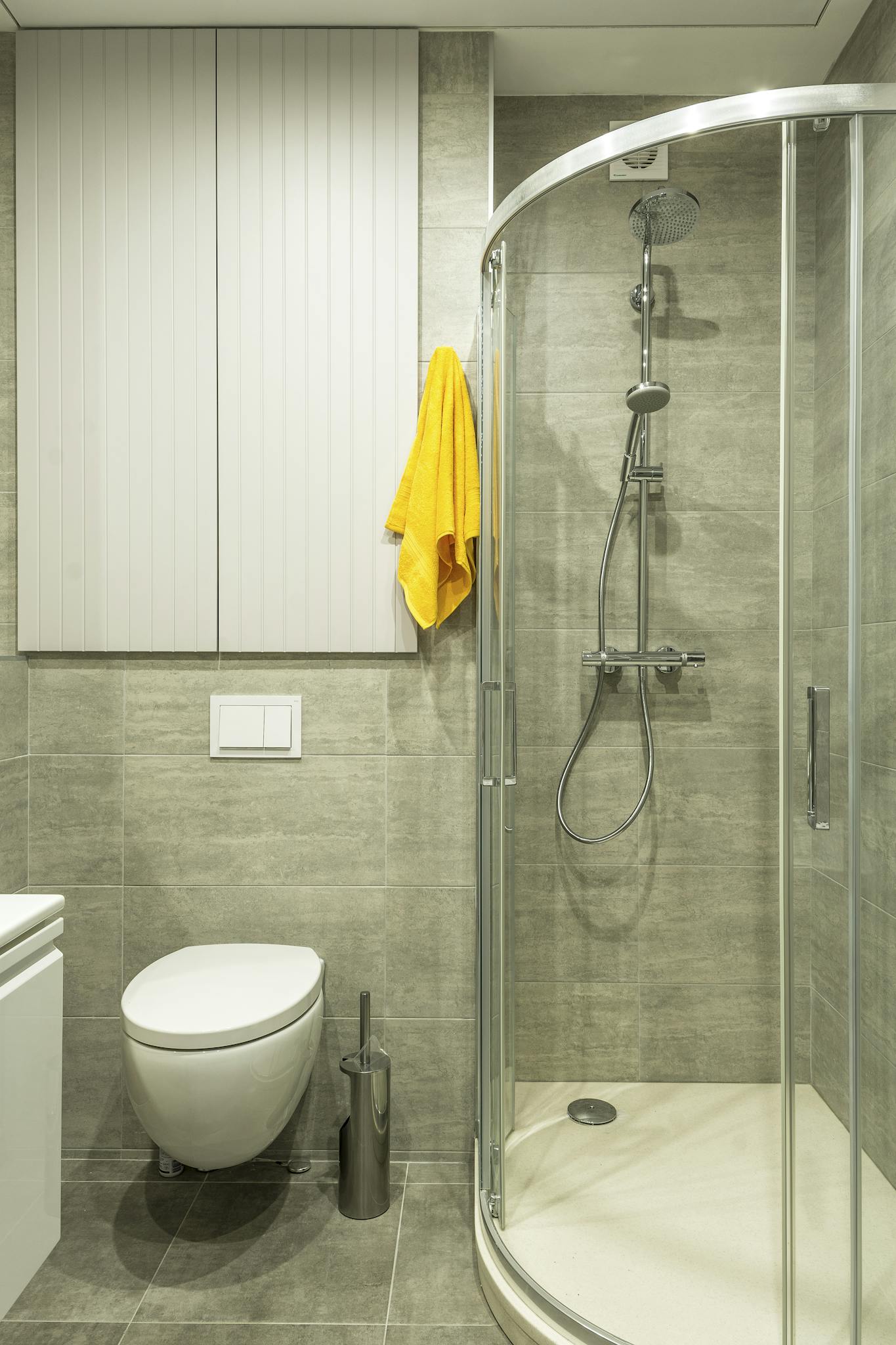 Bright modern bathroom featuring a shower cabin, toilet, and yellow towel for a clean look.